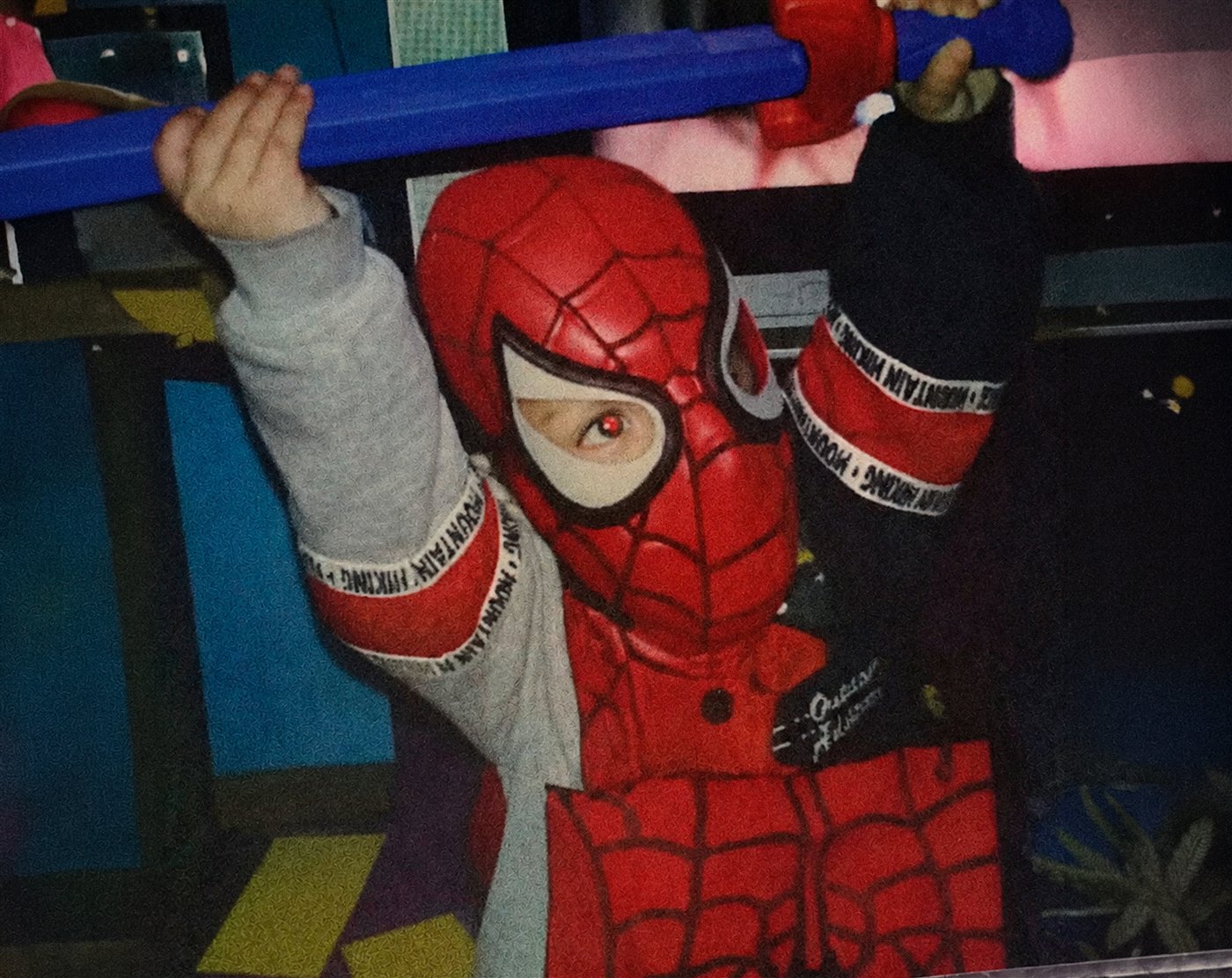Winycius criança, fantasiado de Homem-Aranha, pendurado numa barra azul